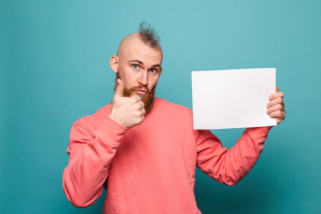 Bearded european man in casual peach isolated, holding white empty paper board thumb up