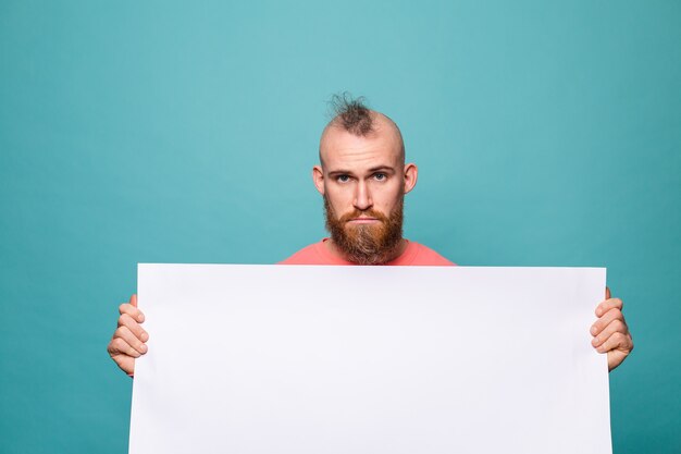 Bearded european man in casual peach isolated, holding white empty paper board with sad unhappy face