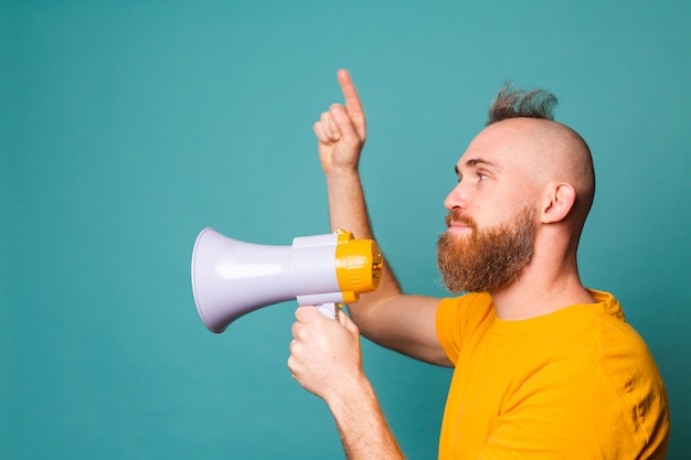 Bearded european man in yellow shirt isolated, crazy shouting in megaphone loudspeaker, attention!