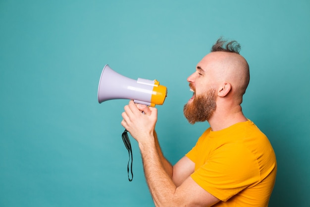 Bearded european man in yellow shirt isolated, crazy shouting in megaphone loudspeaker, attention!