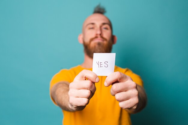 Bearded european man in yellow shirt isolated, holding yes with surprise and amazed expression excited face.