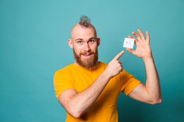 Bearded european man in yellow shirt isolated, holding yes with surprise and amazed expression excited face.