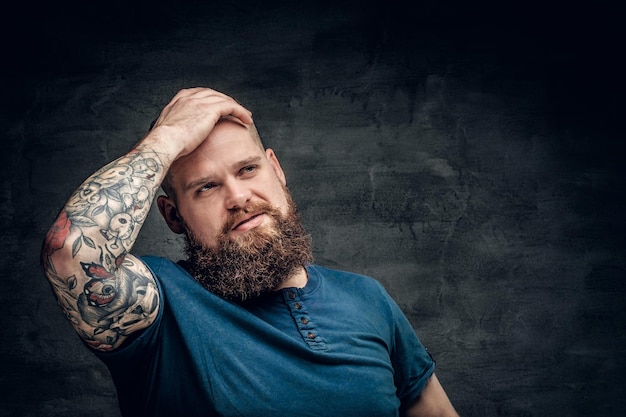 Bearded fat male with tattoo on arms posing over grey background.