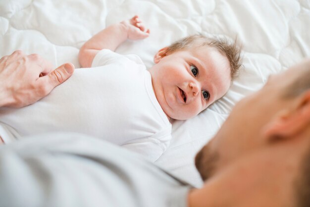 Bearded father lying with baby in white bed