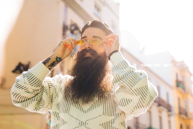 Free photo bearded handsome young man putting on the yellow sunglasses during summer