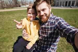 Foto gratuita padre felice barbuto che si siede all'aperto con il suo piccolo figlio