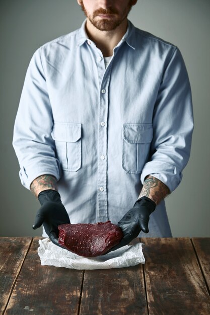 Bearded hipster butcher in black gloves offers piece of whale meat steak