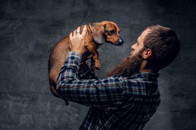 Bearded hipster male in a blue plaid shirt holds in arms brown badger dog.