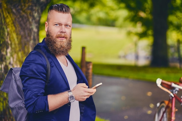 川の近くの公園でスマートフォンを使用してひげを生やしたヒップスターの男性。