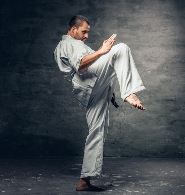 Foto gratuita un combattente di karate barbuto con un tatuaggio sul braccio vestito con un kimono bianco.