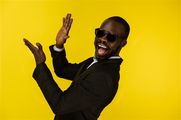 Bearded luxury young afroamerican guy is claping hands in sunglasses and black suit