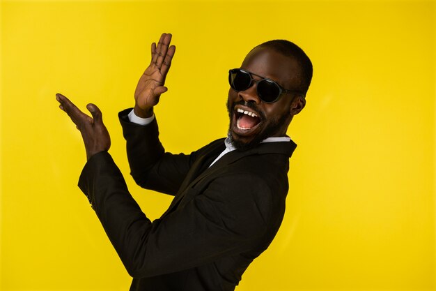 Bearded luxury young afroamerican guy is claping hands in sunglasses and black suit 