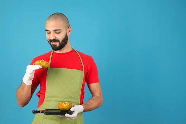 Free photo bearded male chef in apron and gloves holding a dark wooden board with pastry .