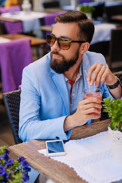 Bearded male drinks, fresh juice at a cafe.