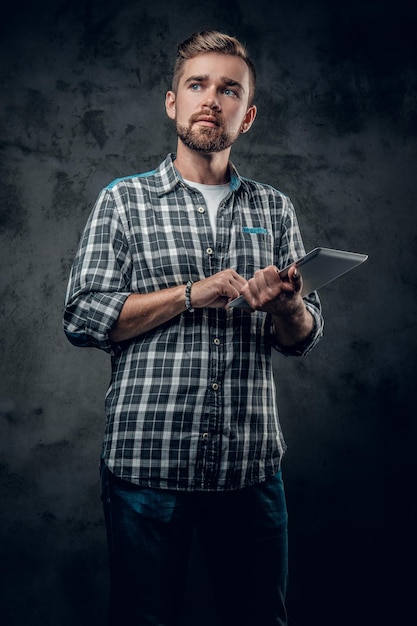 Bearded male in a fleece shirt holds tablet PC over grey background.