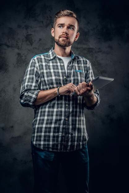 フリースシャツのひげを生やした男性は、灰色の背景の上にタブレットPCを保持します。