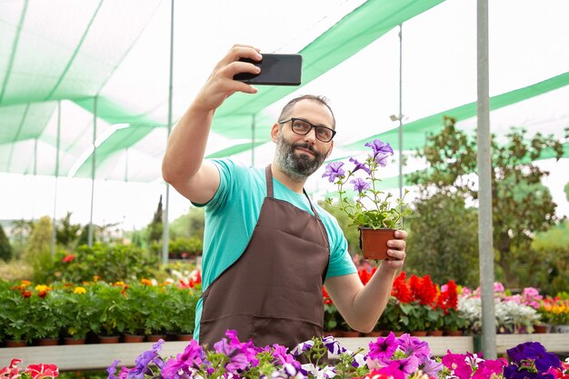 Bearded male gardener taking selfie with potted petunia