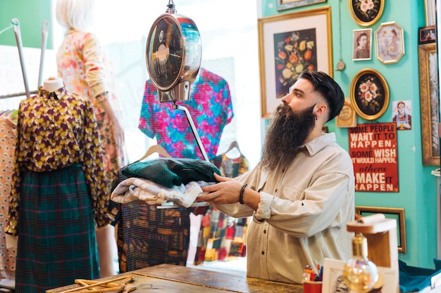 Бородатый мужчина-хозяин проверяет вес ткани на весах в своем магазине одежды