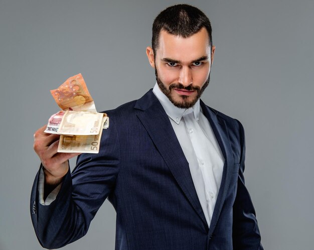 bearded male in a suit holding cash money isolated on grey background.