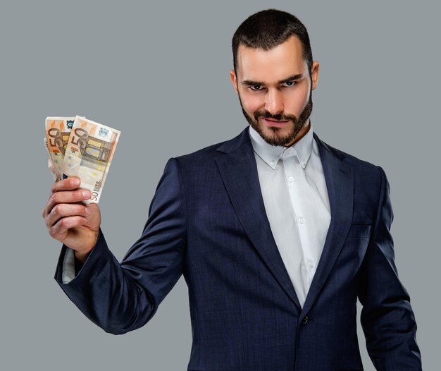 Bearded male in a suit holding cash money isolated on grey background.