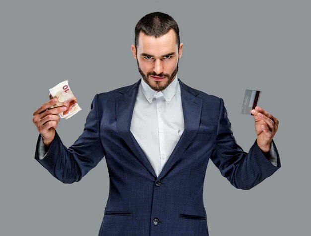 Bearded male in a suit holding cash money isolated on grey background.