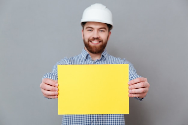 Бородатый мужчина строитель показывает чистый лист бумаги