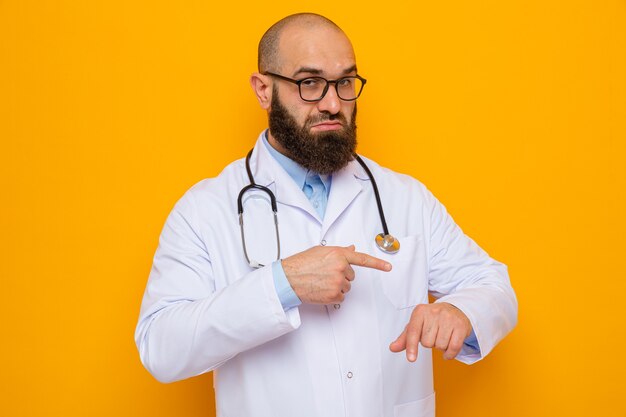 Бородатый мужчина-врач в белом халате со стетоскопом на шее в очках смотрит, указывая пальцем на его руку, напоминая о времени