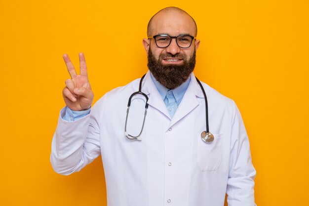 Bearded man doctor in white coat with stethoscope around neck wearing glasses looking smiling cheerfully showing v-sign