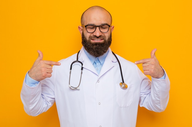 Bearded man doctor in white coat with stethoscope around neck wearing glasses smiling confident pointing at himself