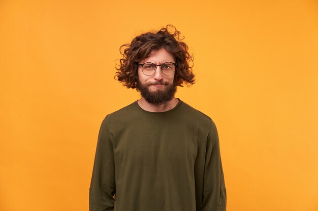 A bearded man in glasses with dark curly hair looking at the front with a frustrated expression of his face