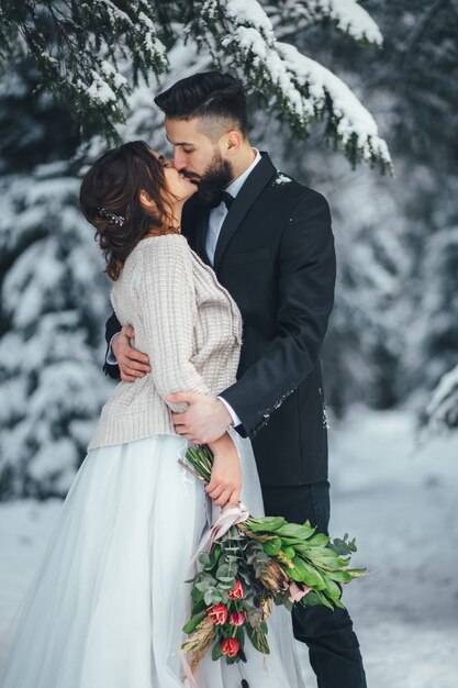 Bearded man and his lovely bride pose on the snow in a magic winter forest