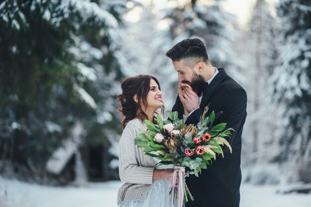 髭の男と彼の素敵な花嫁は魔法の冬の森の雪の上にポーズをとる