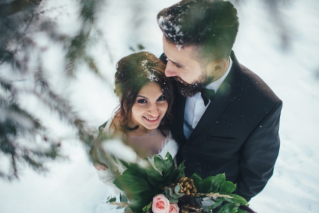 Bearded man and his lovely bride pose on the snow in a magic winter forest