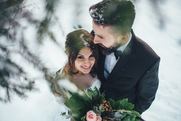 髭の男と彼の素敵な花嫁は魔法の冬の森の雪の上にポーズをとる