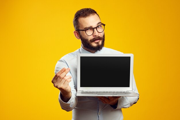 Бородатый мужчина держит ноутбук, показывая денежный жест против