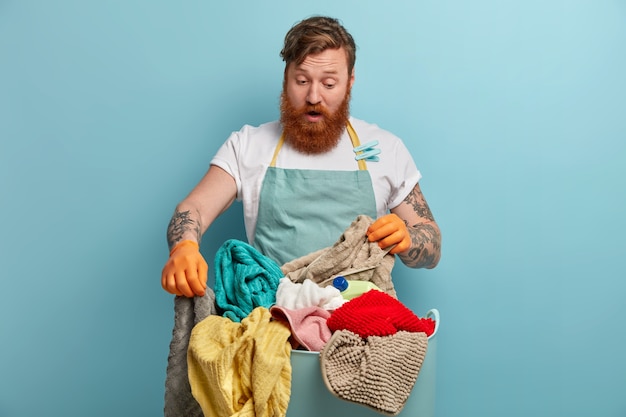 Bearded man holds laundry basket, overwhelmed by household chores