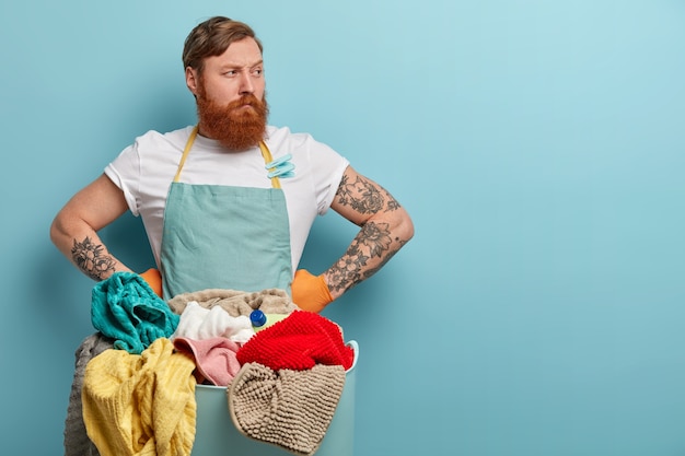 Free photo bearded man holds laundry basket, overwhelmed by household chores