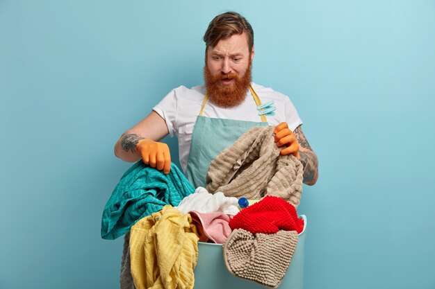Бородатый мужчина держит корзину для белья, перегруженный домашними делами