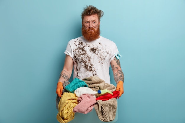 Bearded man holds laundry basket, overwhelmed by household chores