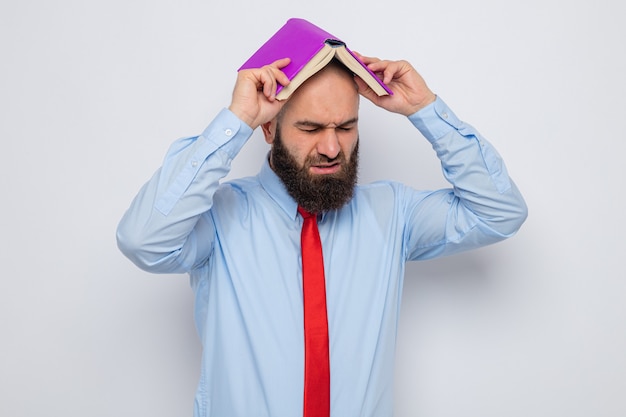 Bearded man in red tie and blue shirt holding book over his head looking tired and annoyed