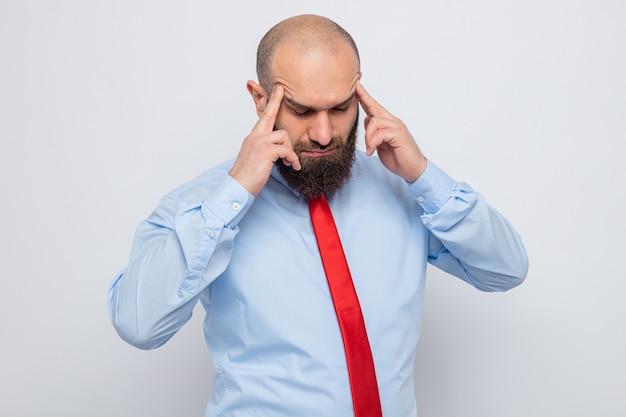 Uomo barbuto in cravatta rossa e camicia blu che si tocca le tempie con le dita che si sente male e soffre di mal di testa