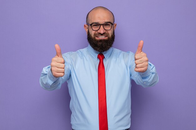 Bearded man in red tie and blue shirt wearing glasses looking happy and positive showing thumbs up