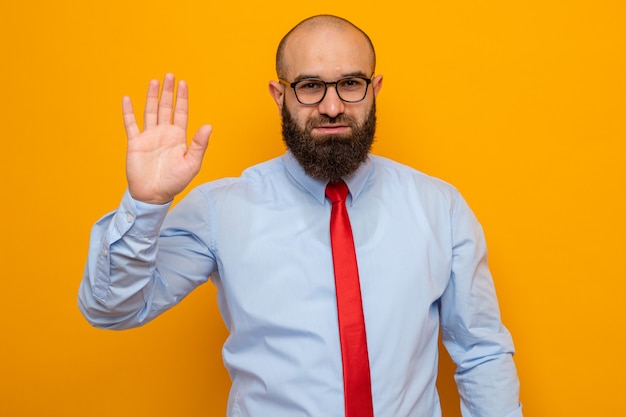 Bearded man in red tie and shirt wearing glasses looking smiling confident waving with hand