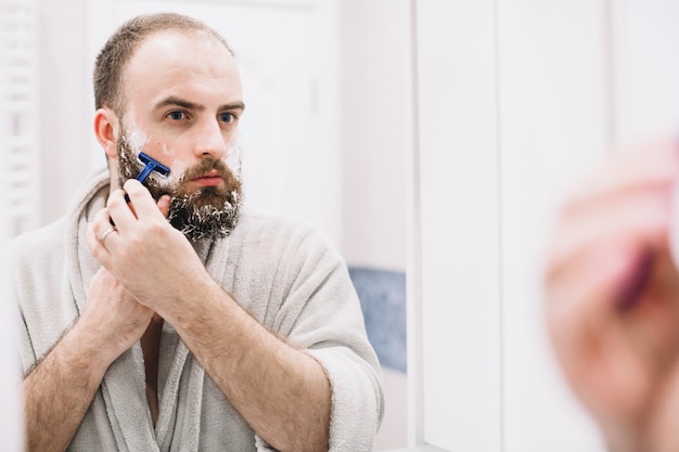 Bearded man shaving in front of mirror