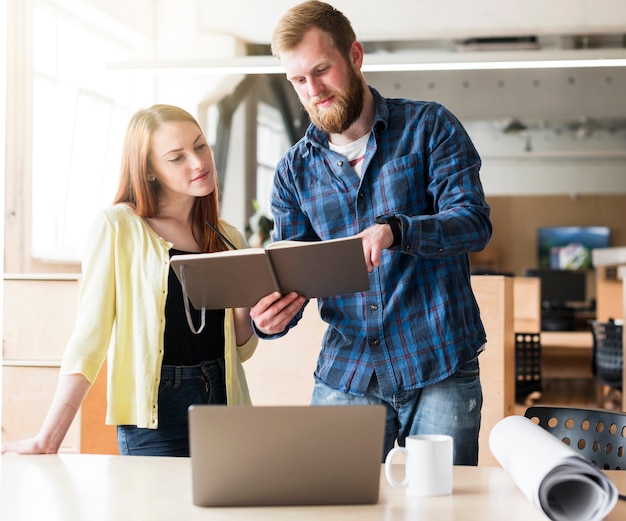 Free photo bearded man showing diary to his beautiful colleague at workplace