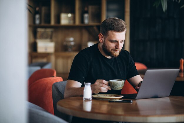 Bearded man sitting in a cafe drinking coffee and working on a computer