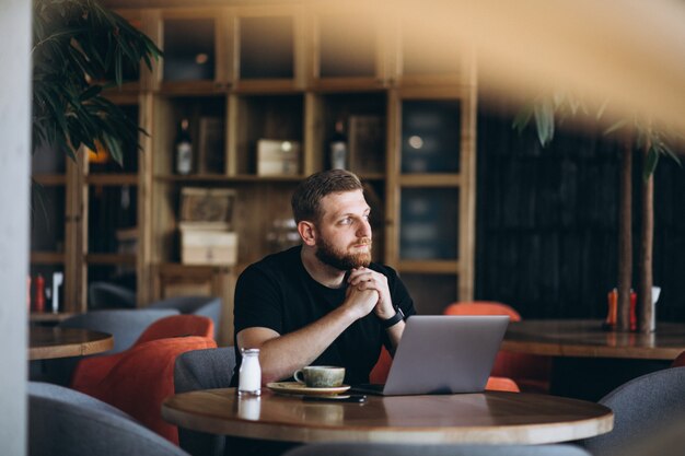 Bearded man sitting in a cafe drinking coffee and working on a computer