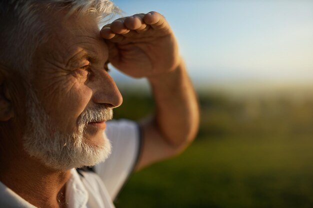 旅行中に遠くを見ながら明るい太陽から目を細めるひげを生やした男性