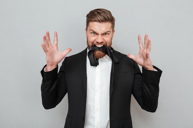 Бородатый мужчина в костюме позирует на сером фоне с галстуком