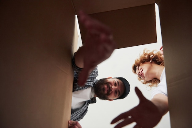 Bearded man trying to reach the item down of a box. Happy couple together in their new house. Conception of moving